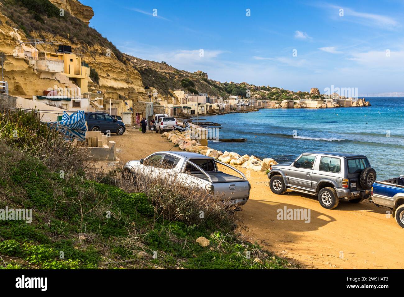 Semplici capanne da pesca si trovano nella baia di Ġnejna vicino a L-Imġarr, Malta, sotto le scogliere, con veicoli lungo il sentiero di accesso sabbioso che porta fino all'acqua. Foto Stock