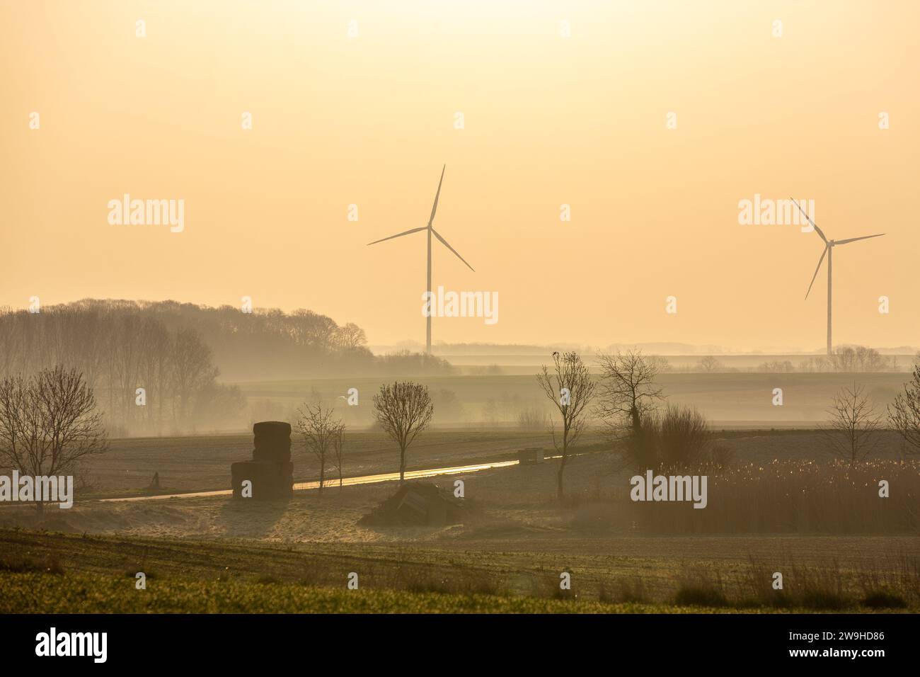 Due turbine eoliche si stagliano contro un cielo arancione all'alba. Foto Stock
