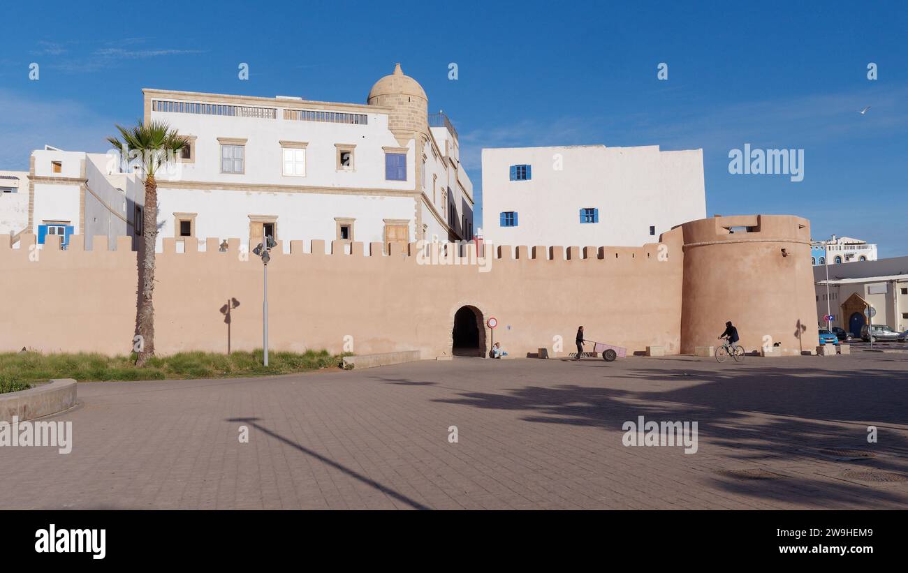 Mura della città e Medina con palme, ciclista e uomo che spingono un carro fuori a Essaouira, Marocco. 28 dicembre 2023 Foto Stock