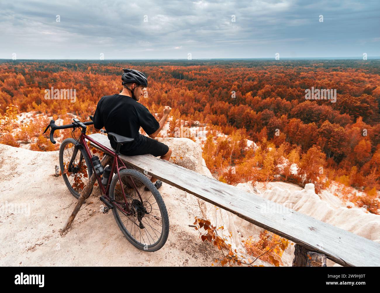 Il ciclista celebra una vittoria stringendo il pugno perché ha raggiunto la sua destinazione. Il ciclista su una panchina di legno con bici in ghiaia guarda l'aut Foto Stock