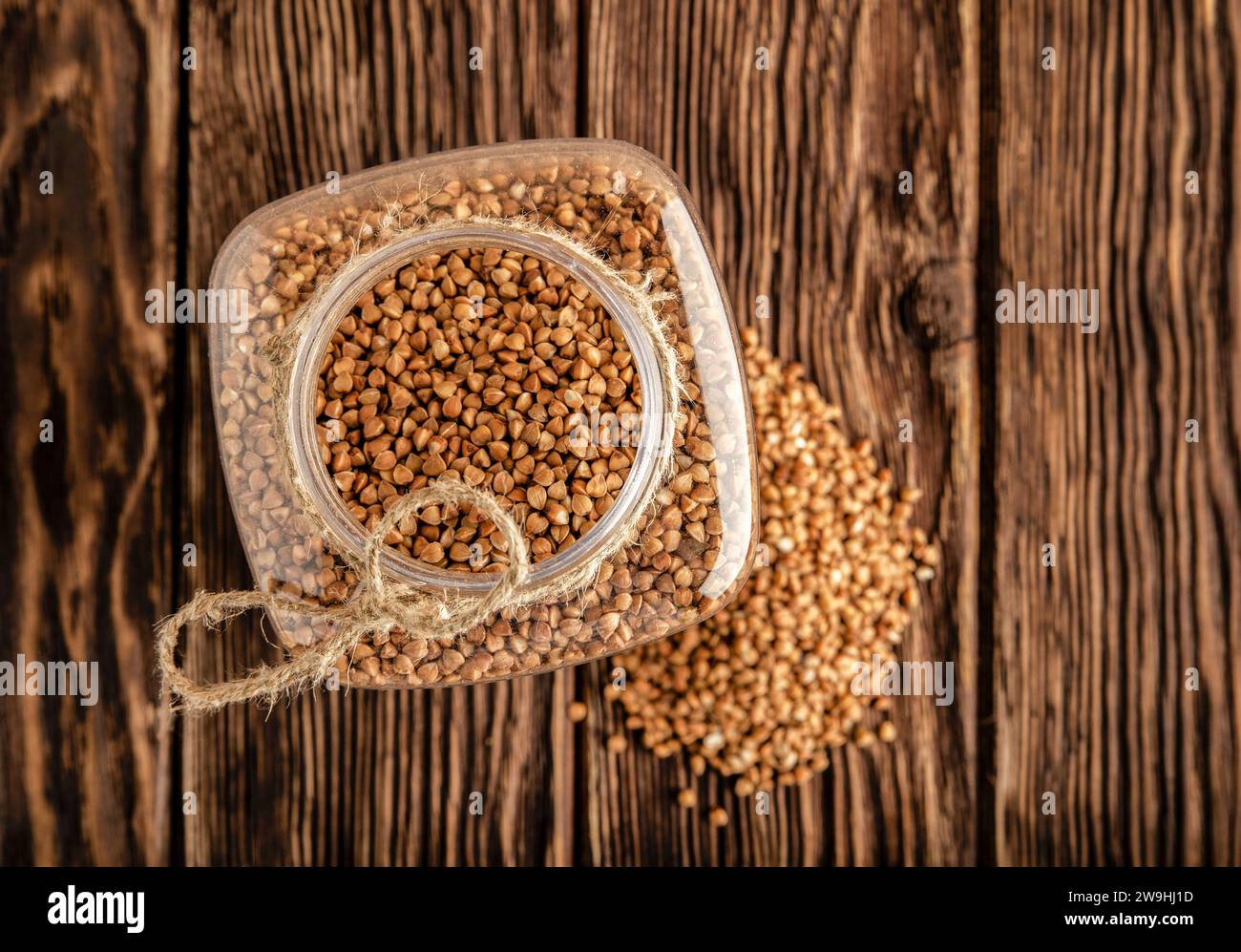 Banco con grano saraceno su fondo di legno. Un mazzo di grano saraceno giace accanto alla lattina. Vista dall'alto. Foto Stock