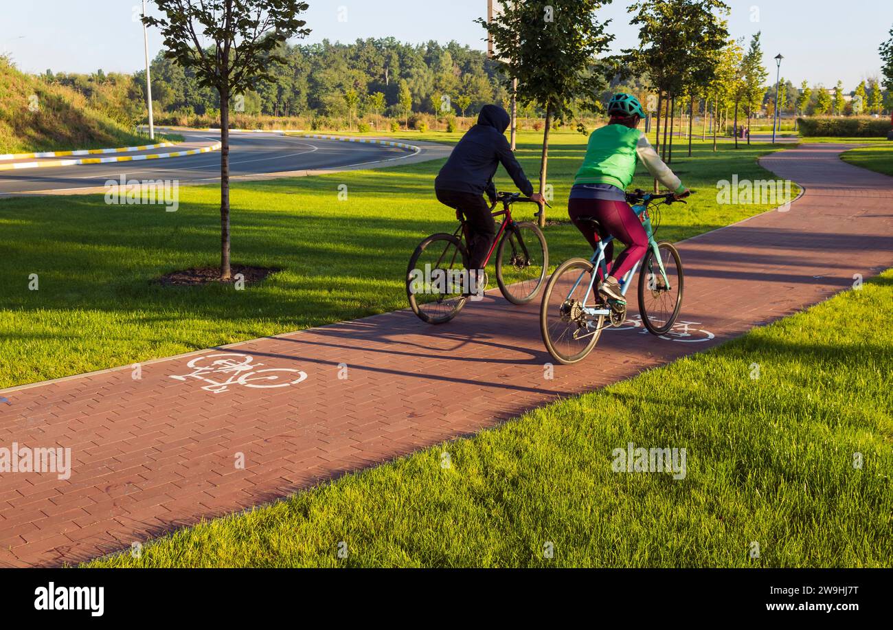 Pista ciclabile nel parco pubblico della città con due ciclisti in sella la mattina presto. Stile di vita attivo. Foto Stock