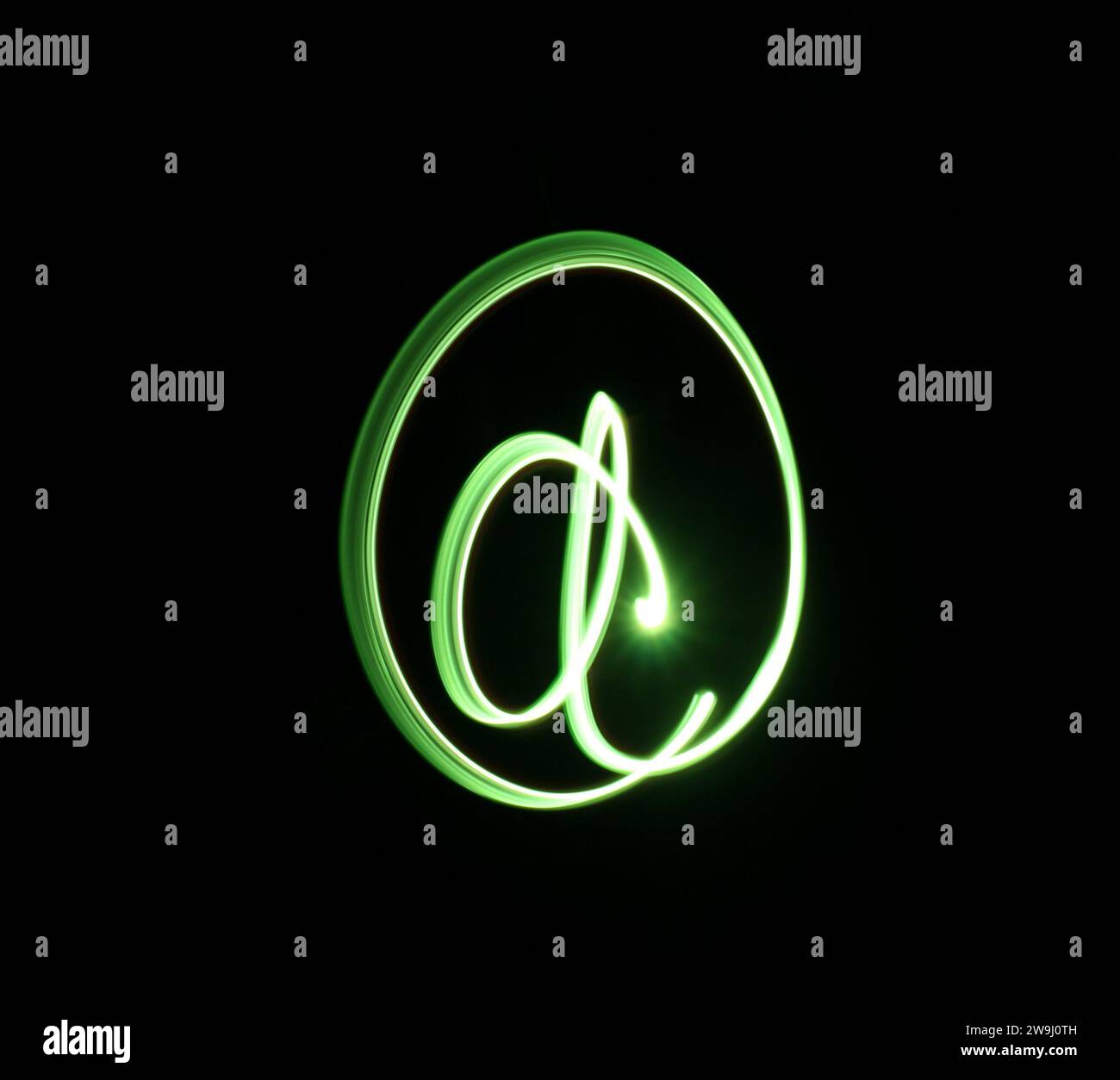 Fotografia di un simbolo "AT" con luce verde brillante in una foto a lunga esposizione su sfondo nero. Fotografia di pittura leggera Foto Stock