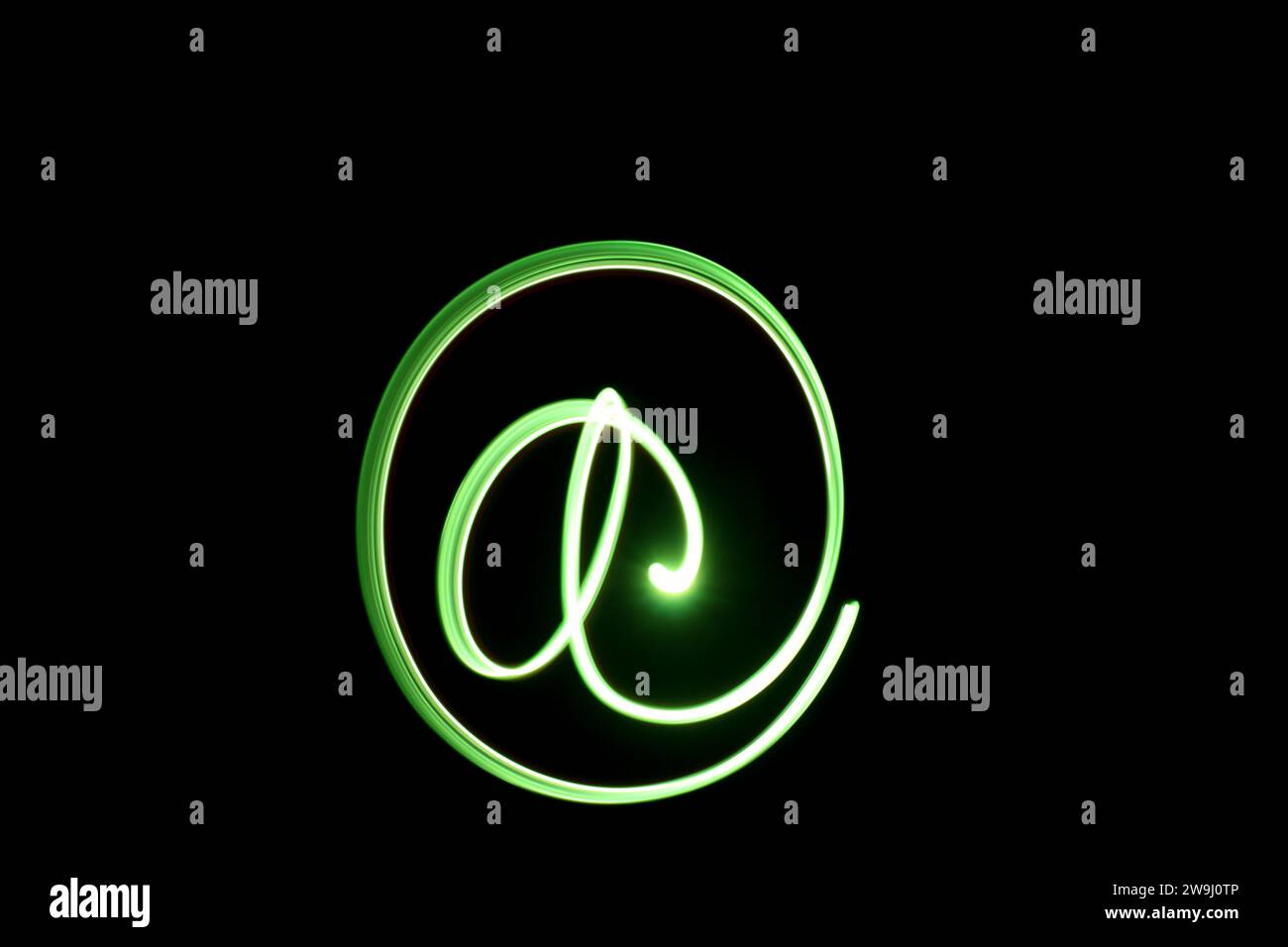 Fotografia di un simbolo "AT" con luce verde brillante in una foto a lunga esposizione su sfondo nero. Fotografia di pittura leggera Foto Stock