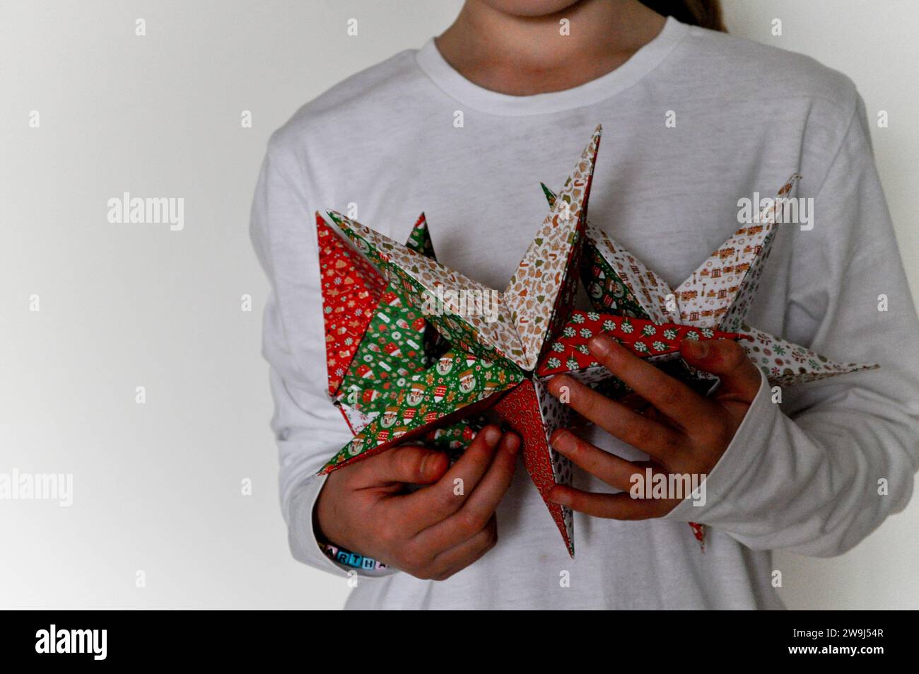 Una foto in studio di un bambino che tiene in mano una collezione di stelle origami realizzata con carta origami festosa Foto Stock