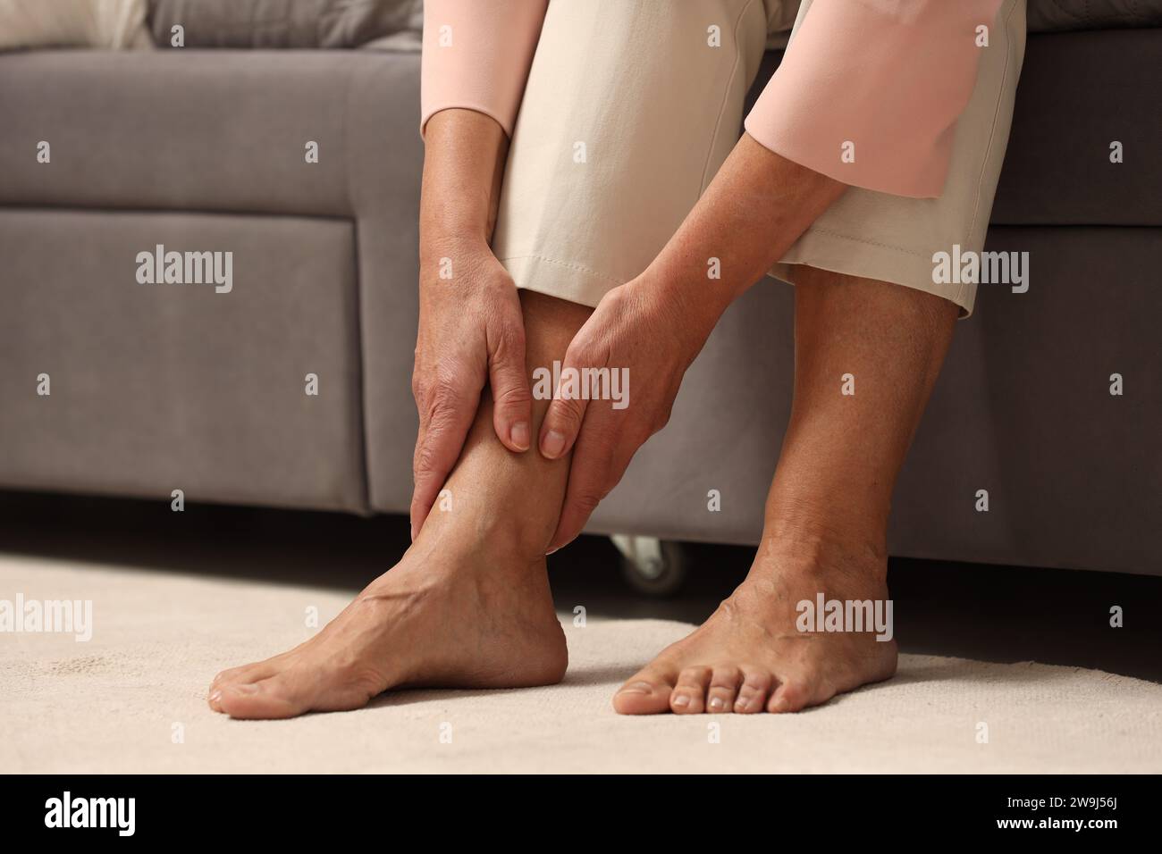 Donna matura che soffre di dolore alle gambe al chiuso, primo piano. Sintomo reumatico Foto Stock