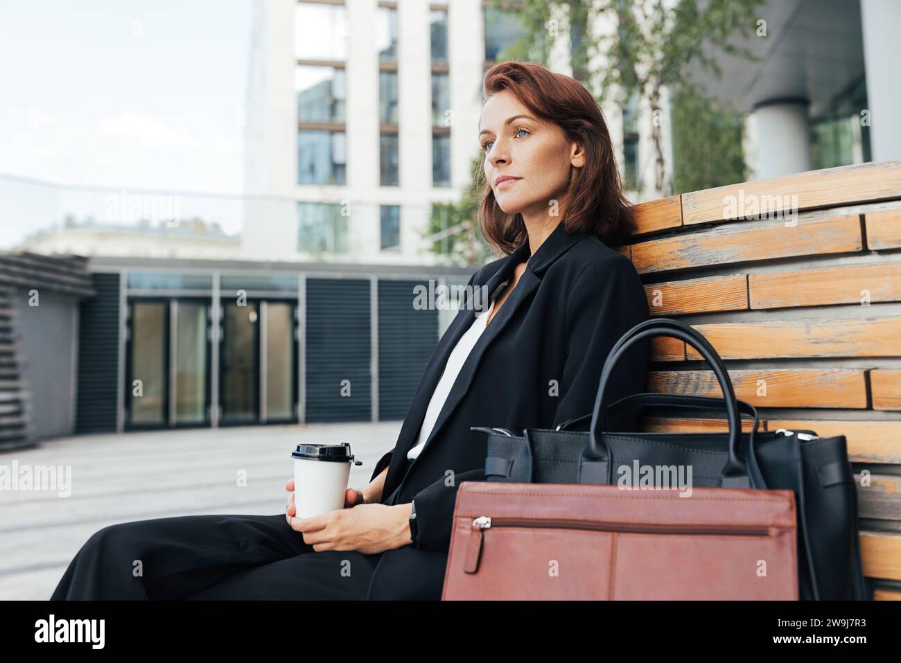 Vista laterale di una donna d'affari di mezza età seduta all'aperto con un caffè Foto Stock