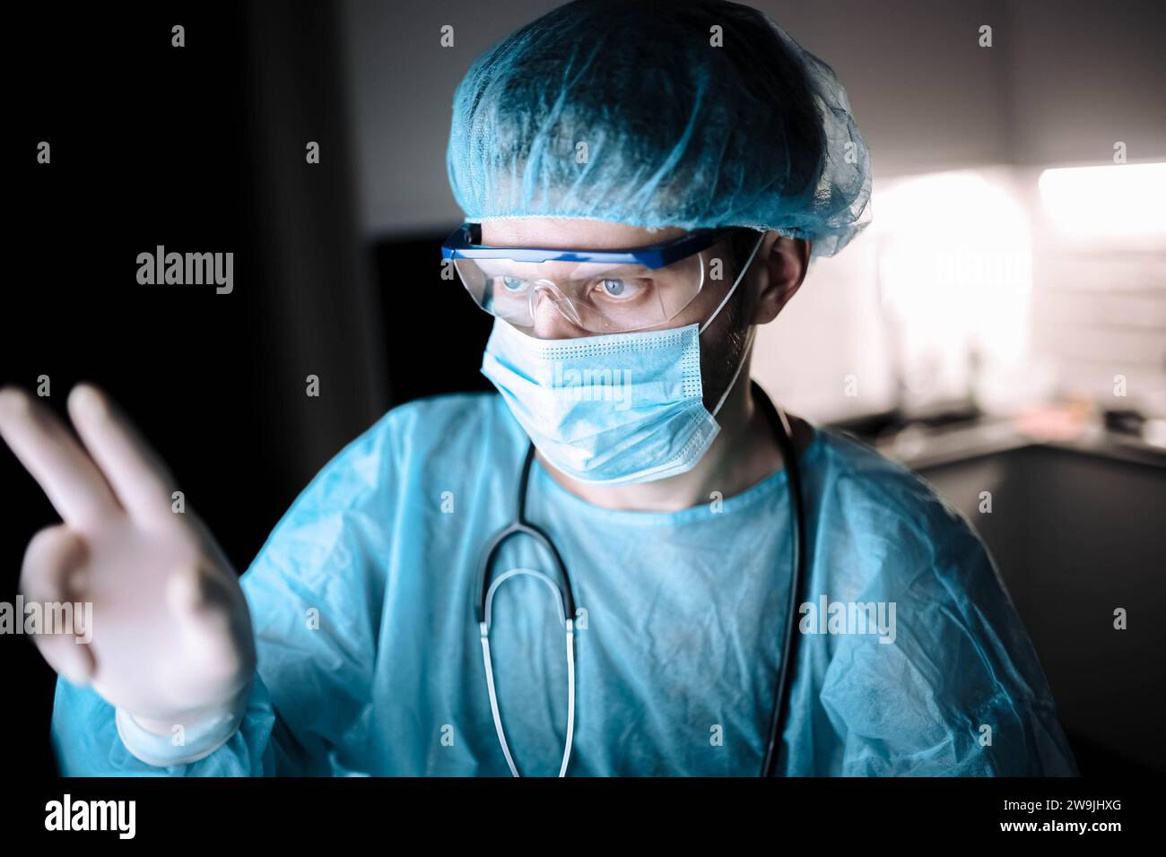 Medico scienziato maschio che lavora in un laboratorio con un monitor in uniforme sterile e occhiali Foto Stock