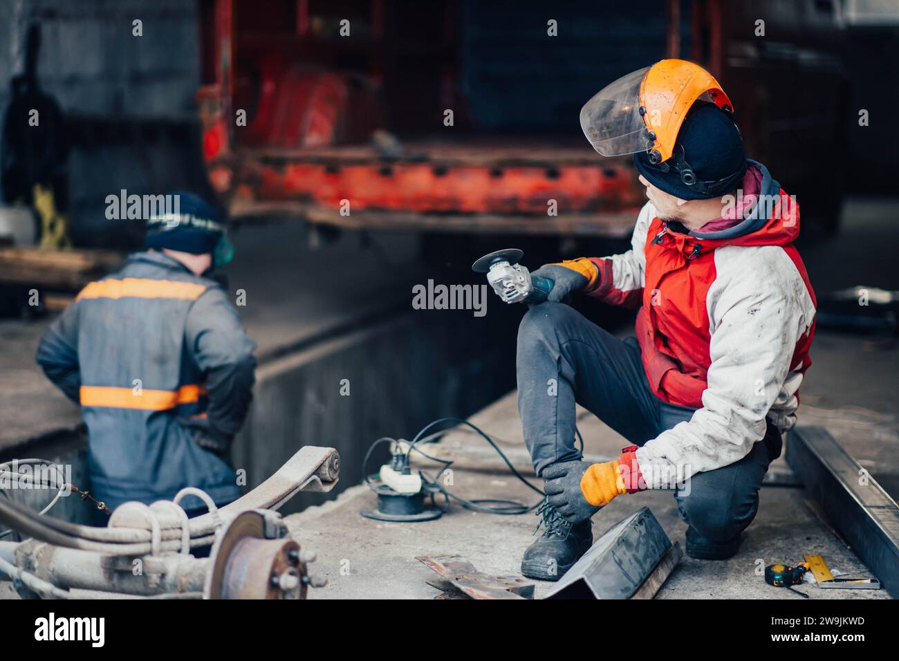 Uomo che lavora in uniforme e maschera lavora con una smerigliatrice, taglia il metallo per la riparazione della carrozzeria di un camion, per la riparazione di un'auto Foto Stock