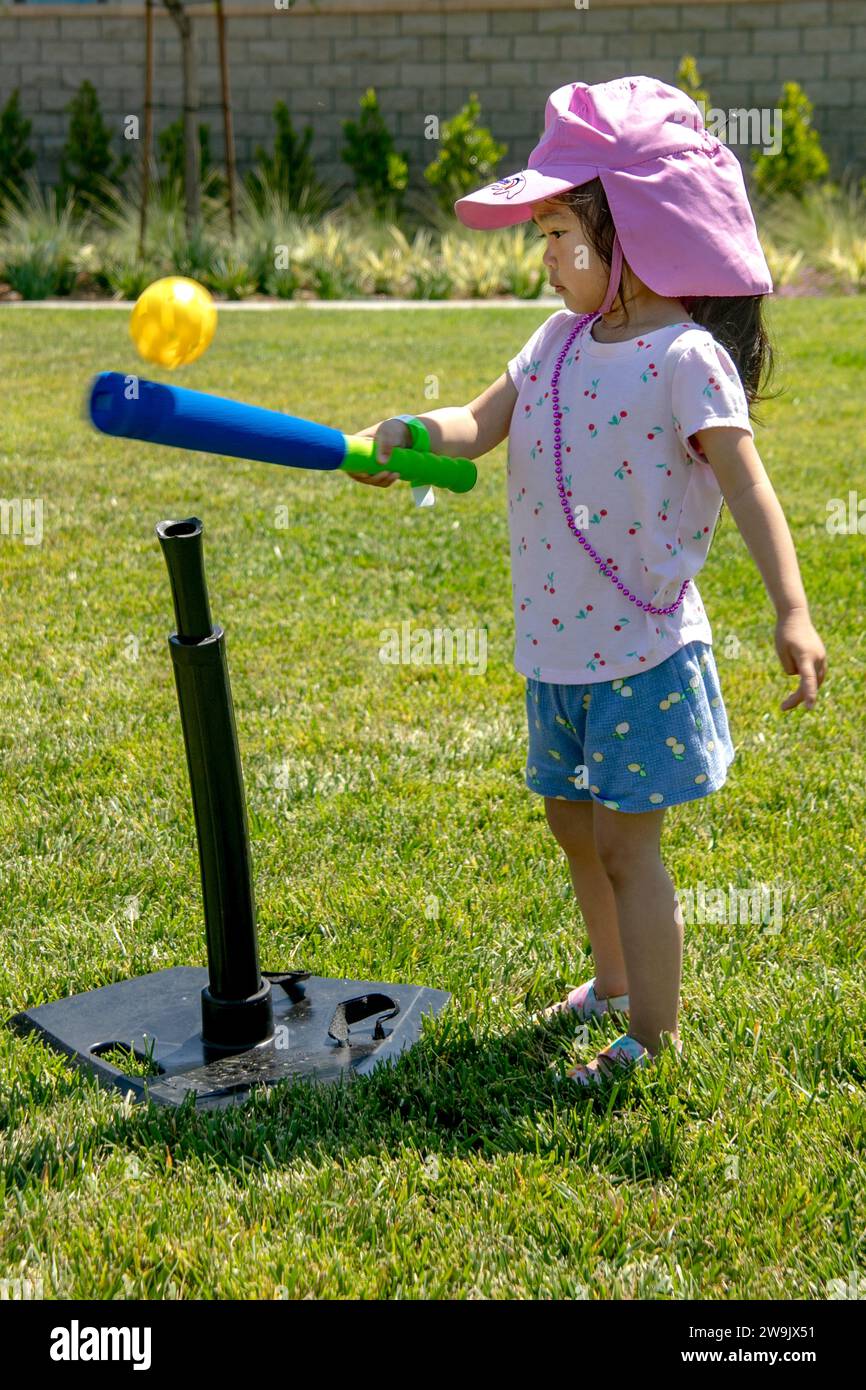 Una bambina asiatica americana di tre anni fa fa fa un'oscillazione prudente con una mazza da pallina Wiffle in un parco di Costa Mesa, CALIFORNIA. Foto Stock