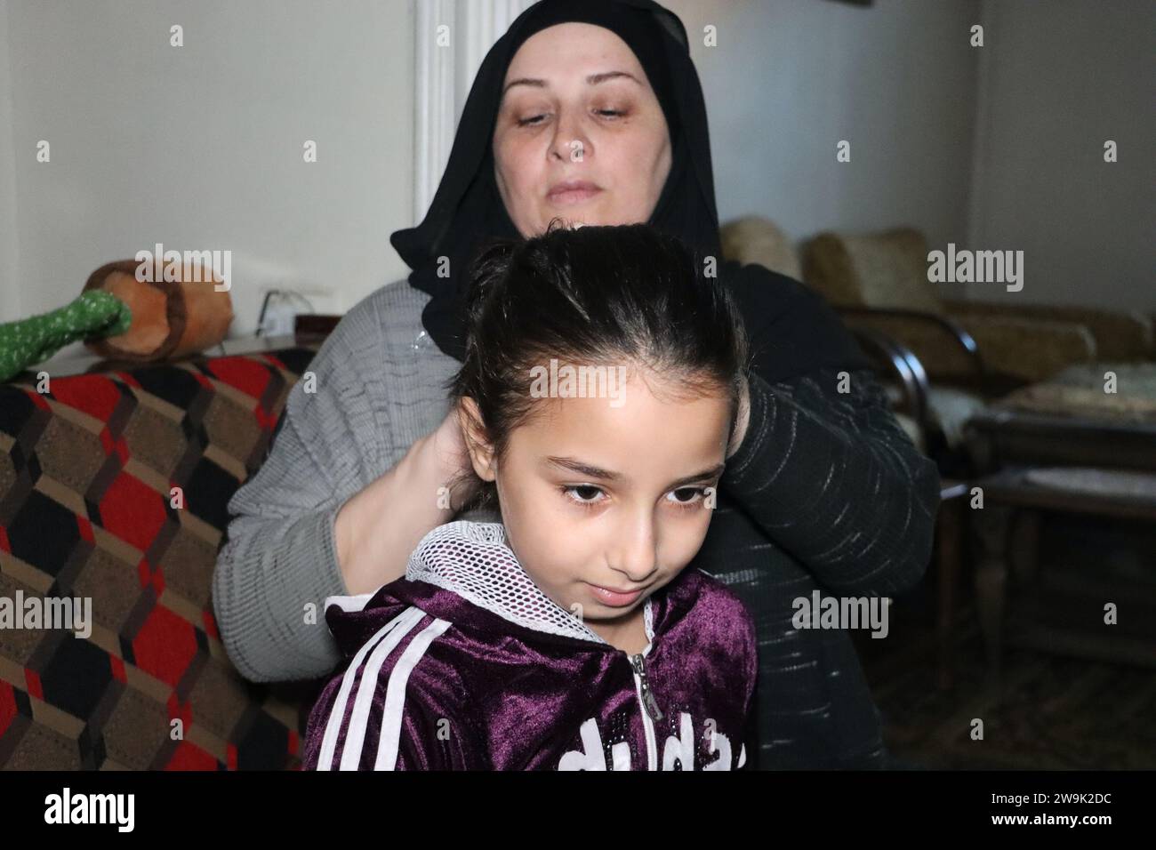 Al Hasakah. 28 dicembre 2023. Al-Batoul Aliwi, un'insegnante di 45 anni, combini per sua figlia a casa nella provincia di al-Hasakah, nel nord-est della Siria, il 28 dicembre 2023. Nel cuore della città di al-Hasakah nel nord-est della Siria, una famiglia di sei lotte sotto il peso delle sfide imposte dalla presenza delle forze statunitensi nel nord-est e nella Siria orientale. Crediti: Str/Xinhua/Alamy Live News Foto Stock