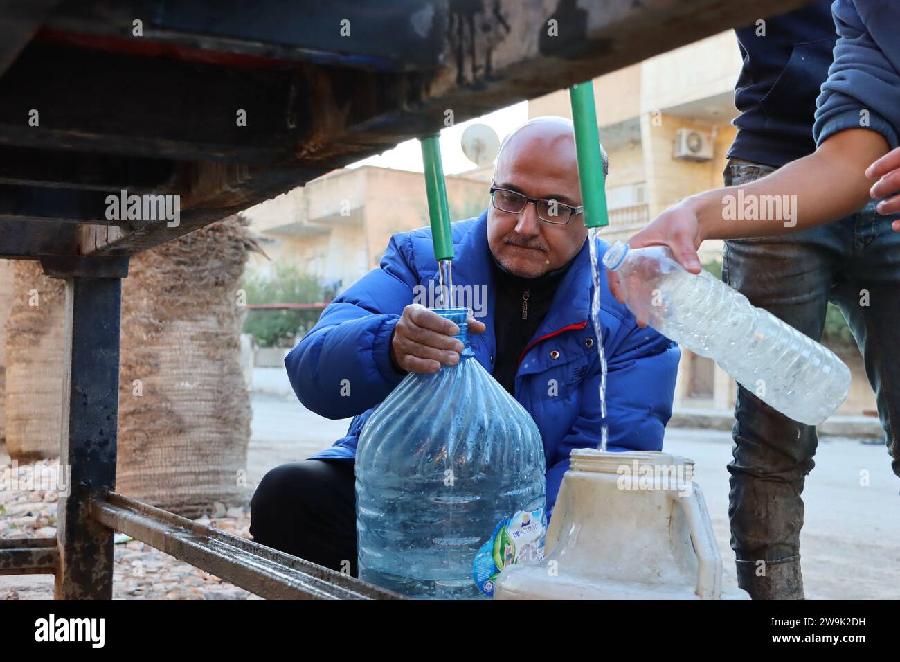 Al Hasakah. 28 dicembre 2023. Ghassan al-Hamoud, un insegnante di 51 anni, riempie un contenitore di plastica con acqua nella provincia di al-Hasakah, nel nord-est della Siria, il 28 dicembre 2023. Nel cuore della città di al-Hasakah nel nord-est della Siria, una famiglia di sei lotte sotto il peso delle sfide imposte dalla presenza delle forze statunitensi nel nord-est e nella Siria orientale. Crediti: Str/Xinhua/Alamy Live News Foto Stock