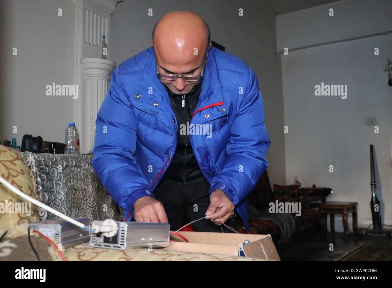 Al Hasakah. 28 dicembre 2023. Ghassan al-Hamoud, un insegnante di 51 anni, collega una piccola batteria per generare elettricità a casa nella provincia di al-Hasakah, nel nord-est della Siria, il 28 dicembre 2023. Nel cuore della città di al-Hasakah nel nord-est della Siria, una famiglia di sei lotte sotto il peso delle sfide imposte dalla presenza delle forze statunitensi nel nord-est e nella Siria orientale. Crediti: Str/Xinhua/Alamy Live News Foto Stock