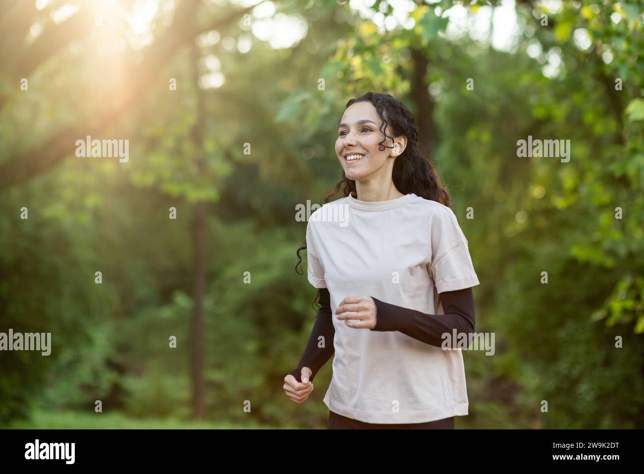 Giovane bella donna che corre la sera nel parco, donna ispanica con i capelli ricci sorridente e vivace stile di vita Foto Stock