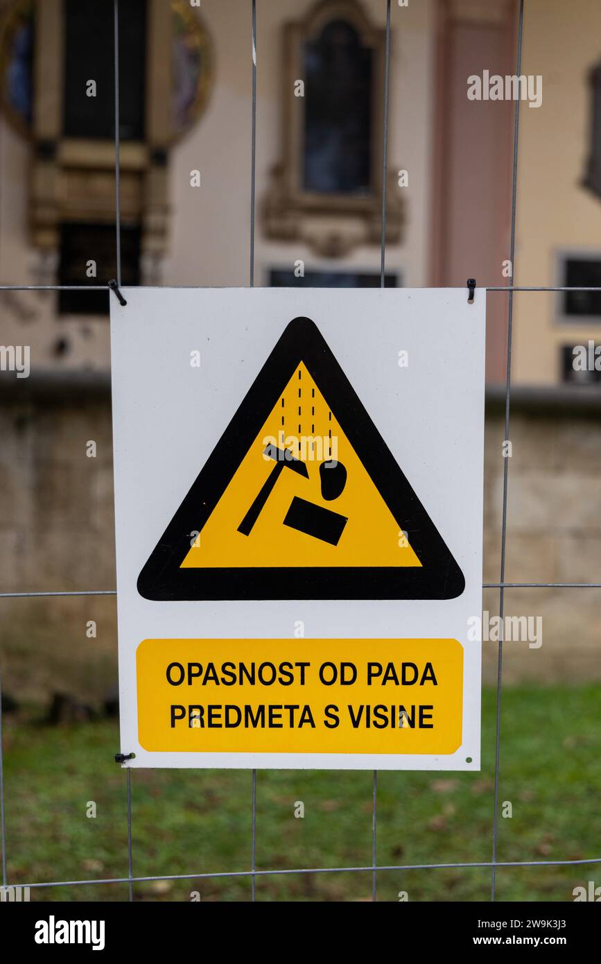 Segnale di avvertimento (triangolo giallo) su una recinzione intorno al cantiere (in un cimitero): Pericolo di caduta di oggetti dall'alto (testo in lingua croata) Foto Stock