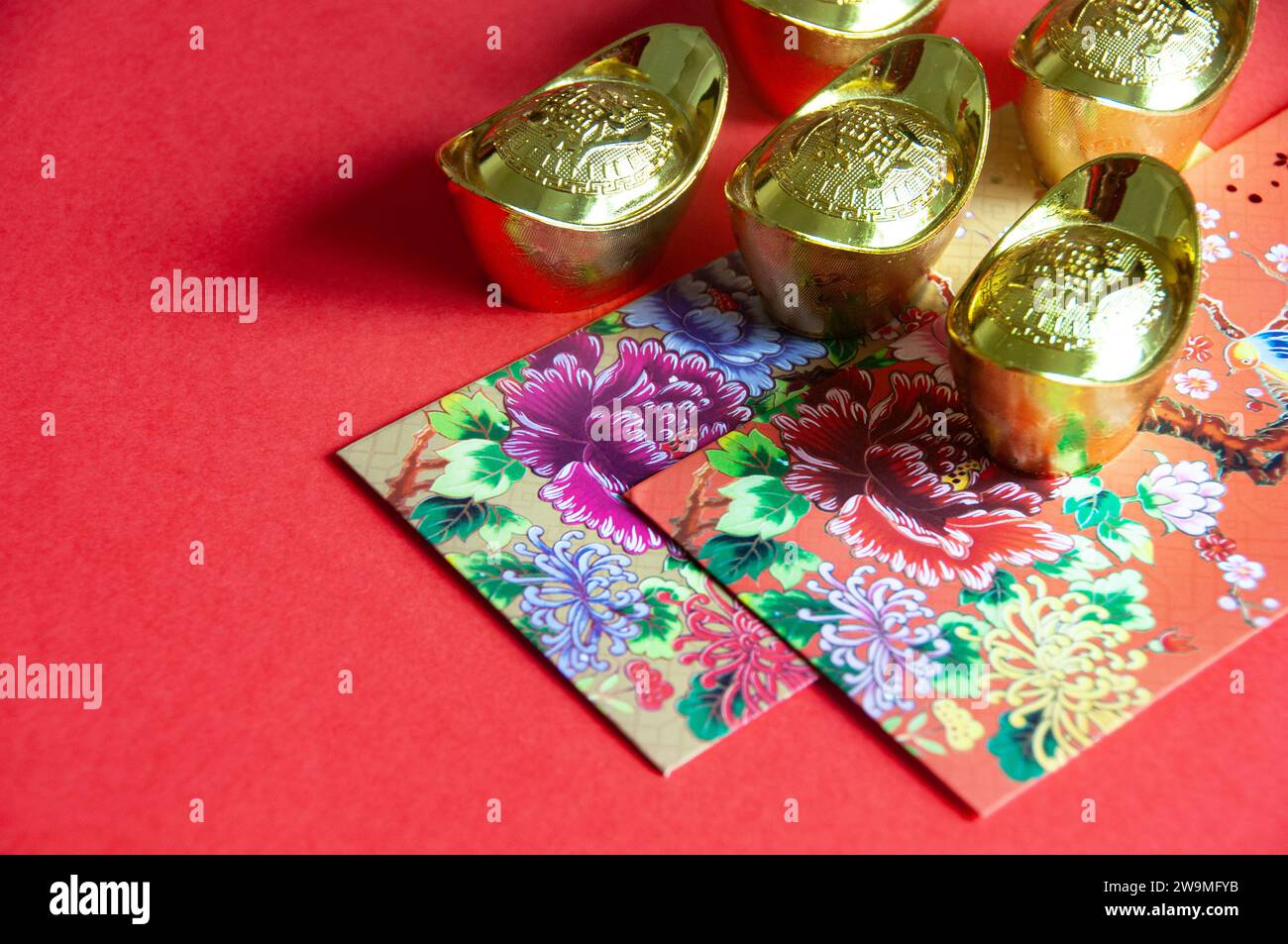 Busta colorata e lingotti dorati su sfondo rosso con auguri di Capodanno cinese. Foto Stock