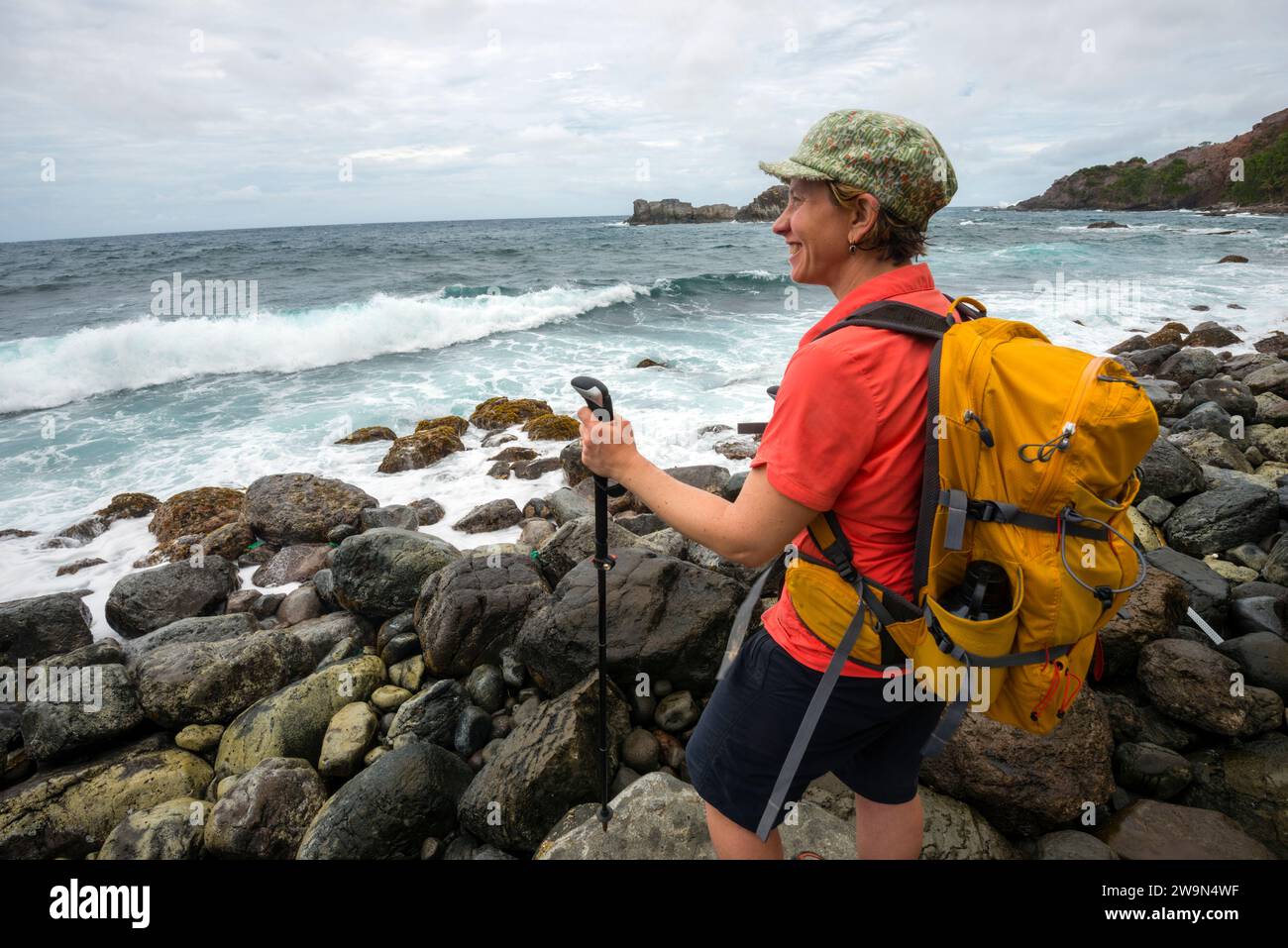 Un escursionista con zaino in spalla si affaccia sull'Oceano Atlantico mentre fa trekking nel segmento 6 del Waitukubuli National Trail sull'isola caraibica di Dominica. Foto Stock