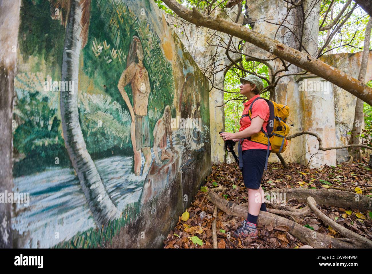 Uno zaino in spalla guarda un murale tra le rovine di una vecchia chiesa nel territorio di Kalinago nel segmento 6 del Waitukubuli National Trail sull'isola caraibica di Dominica. La chiesa Foto Stock