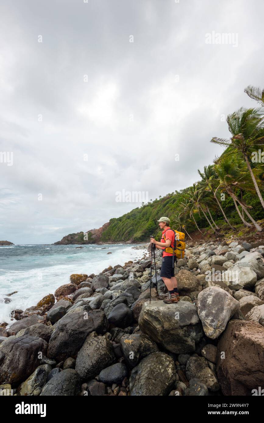 Un escursionista con zaino in spalla si affaccia sull'Oceano Atlantico mentre fa trekking nel segmento 6 del Waitukubuli National Trail sull'isola caraibica di Dominica. Foto Stock