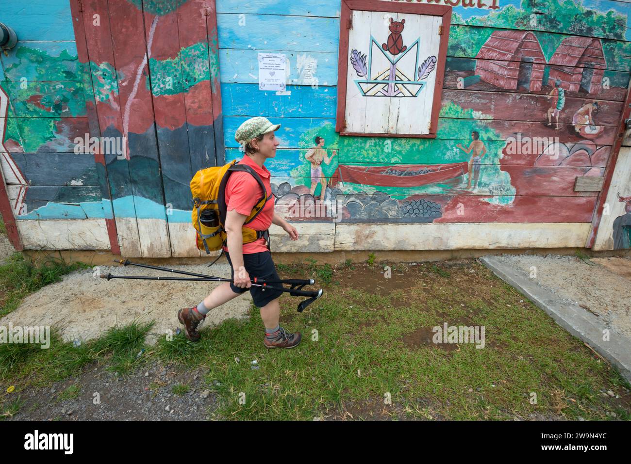 Un escursionista con zaino in spalla in un edificio colorato nel territorio di Kalinago nel segmento 6 del Waitukubuli National Trail sull'isola caraibica di Dominica. Foto Stock
