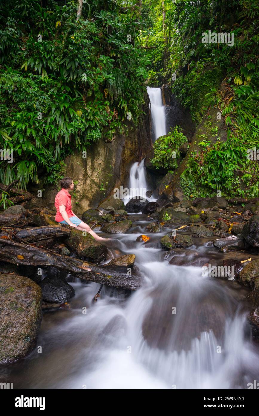 Una donna si rilassa davanti a una splendida cascata a Trafalgar presso il papillote Wilderness Retreat al termine del segmento 3 del Waitukubuli National Trail sull'isola caraibica di Foto Stock