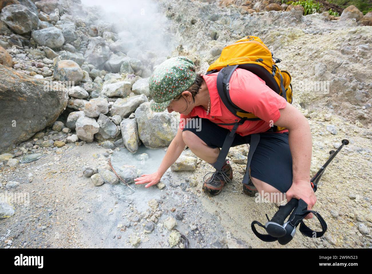 Una donna sente il calore che fuoriesce dalle calde piscine di solfo nella Valle della Desolazione mentre si dirige verso il lago bollente sull'isola caraibica di Dominica. Foto Stock