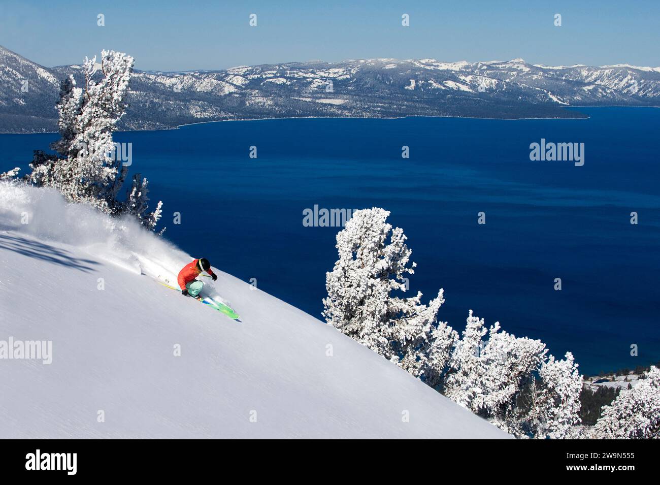 Una sciatrice (Hazel Birnbaum) scierà in neve profonda in una splendida giornata all'Heavenly Mountain Resort con il lago Tahoe sullo sfondo vicino al South Lake Tahoe, California. Foto Stock