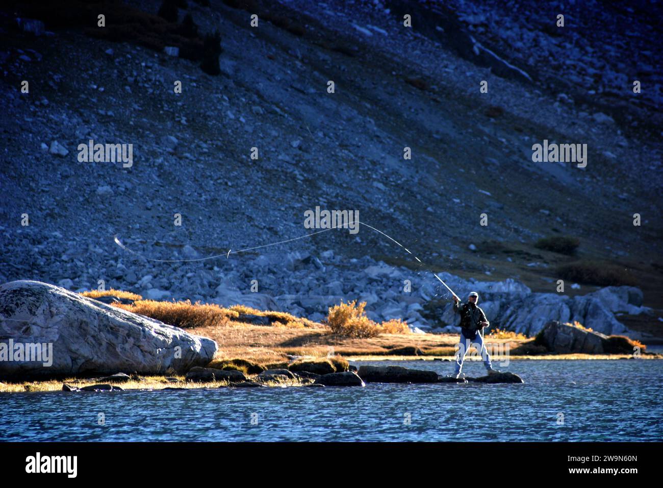 Un uomo fa oscillare la canna da mosca, catturando la luce del sole su di essa, pescando vicino al lago Saddlebag, nelle Sierra Mountains orientali della California. Foto Stock