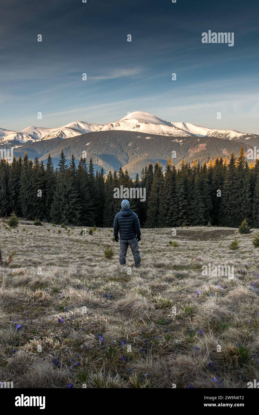 Giovane uomo in abiti caldi in piedi sulle montagne all'alba Foto Stock