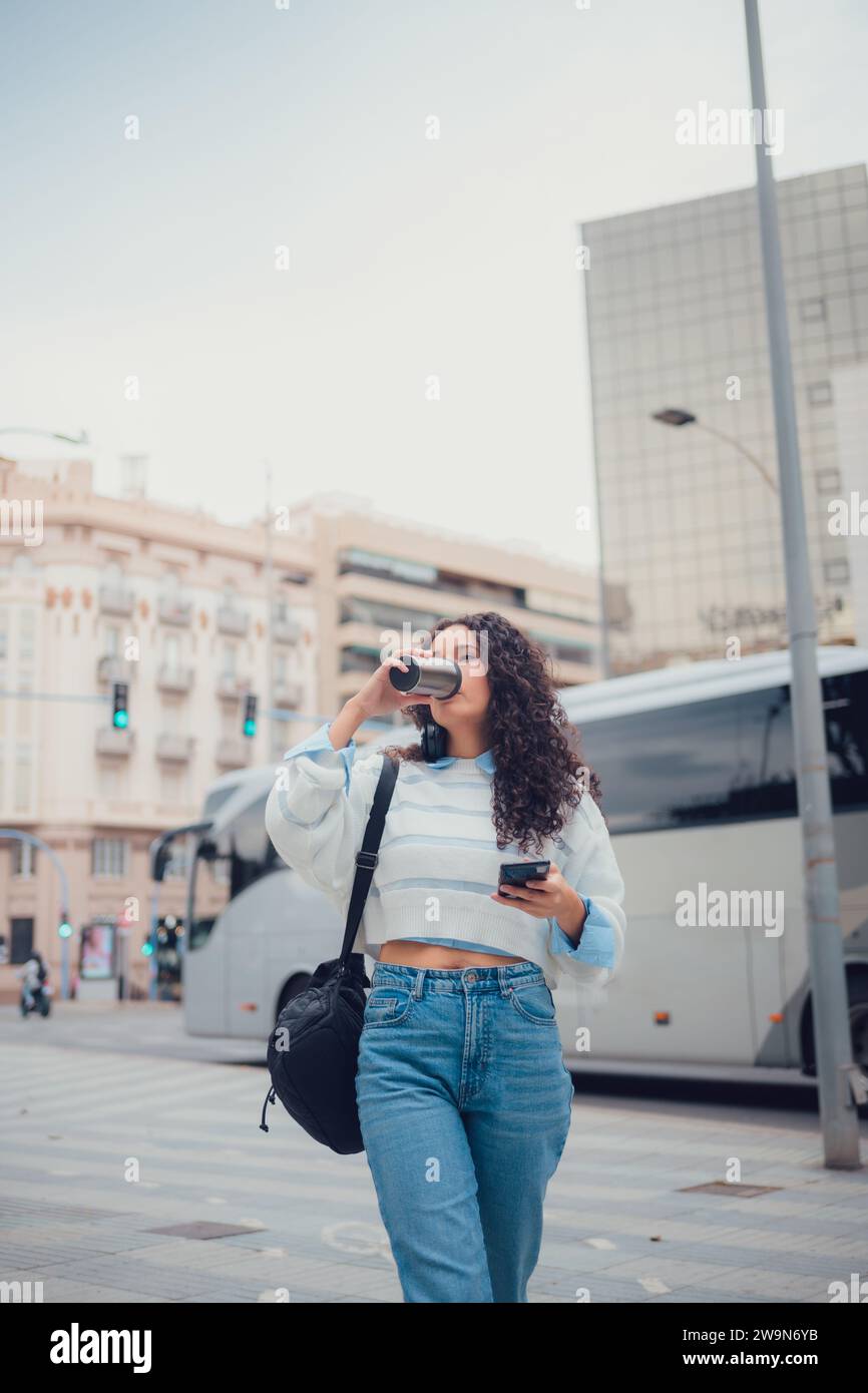 Donna sudamericana con capelli ricci che beve caffè per strada Foto Stock