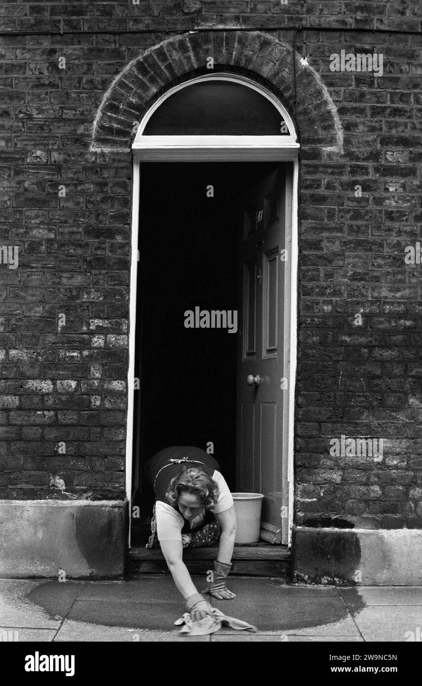 Classe operaia Londra Regno Unito anni '1970 Una casa orgogliosa residente lava il gradino della porta d'ingresso e il marciapiede, creando una separazione dalla sporcizia quotidiana e dalla virtuosa pulizia dell'interno. Roupell Street Waterloo, Londra, Inghilterra 1975 HOMER SYKES . Foto Stock