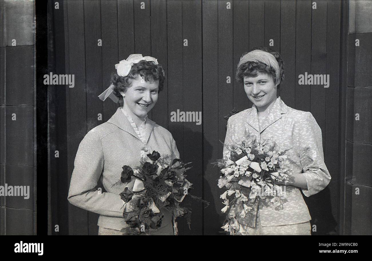 Anni '1950, storico, matrimonio, due belle ragazze, sorelle, sulla sinistra una sposa con la sua damigella d'onore all'ingresso della chiesa in piedi con mazzi di fiori, Inghilterra Regno Unito. Foto Stock