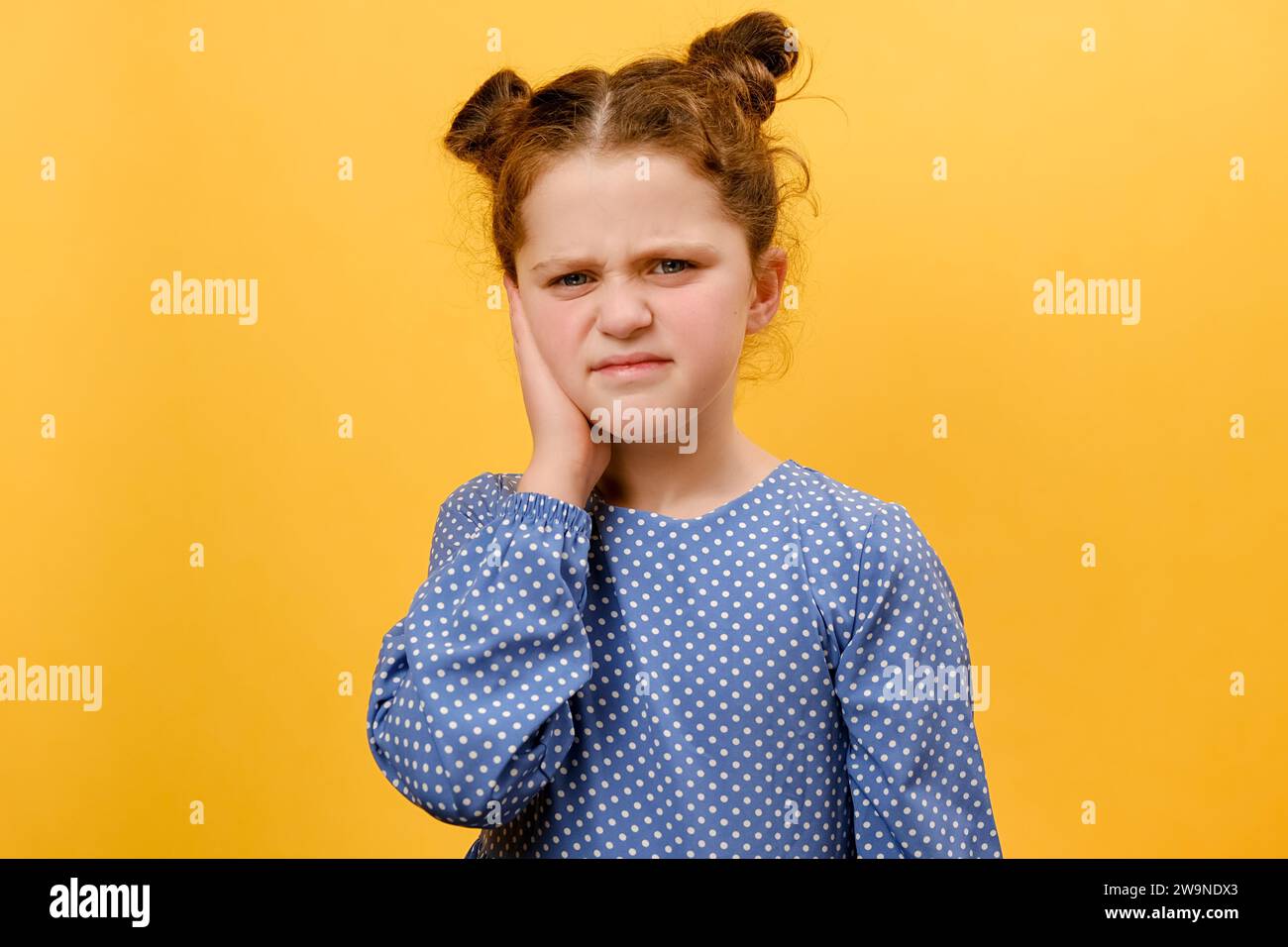Ritratto di una infelice bambina preadolescente che soffre di dolore all'orecchio, in posa isolata sulla parete di sfondo di colore giallo in studio. La causa del mal d'orecchio include Foto Stock