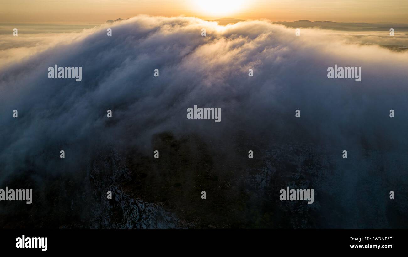 Sicilia 2023. Nuvole che si arrampicano sul Monte Santa Caterina sull'isola di Favignana. Dietro vediamo il sole all'alba. Luglio 2023 Trapani, Italia Foto Stock
