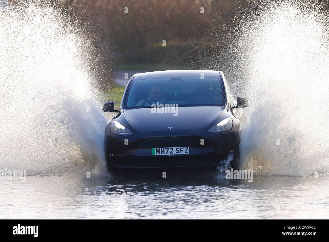 Un'auto elettrica che ha fatto un grande salto mentre viaggia attraverso una strada allagata a Fairburn, North Yorkshire, Regno Unito Foto Stock