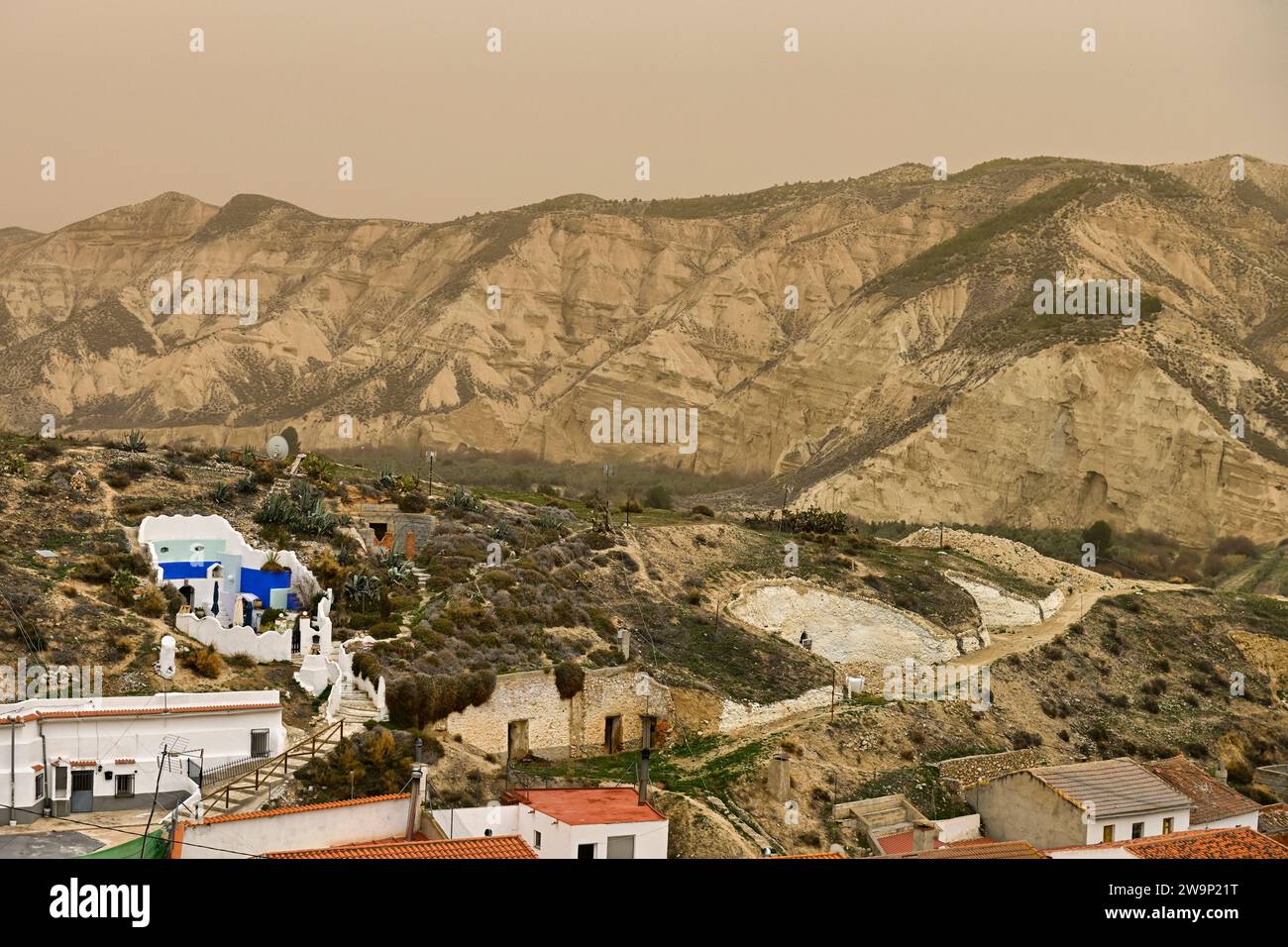 Case in grotta con distintive porte blu immerse in un aspro paesaggio montano nel deserto. Foto Stock