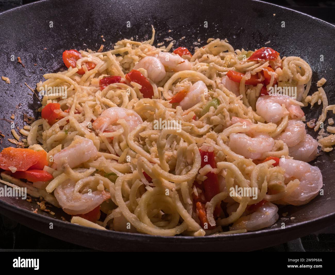 Crepuscoli di zucca a spirale che ballano con gamberi sfrigolanti e vivaci peperoni rossi in una teglia di ghisa stagionata. Foto Stock