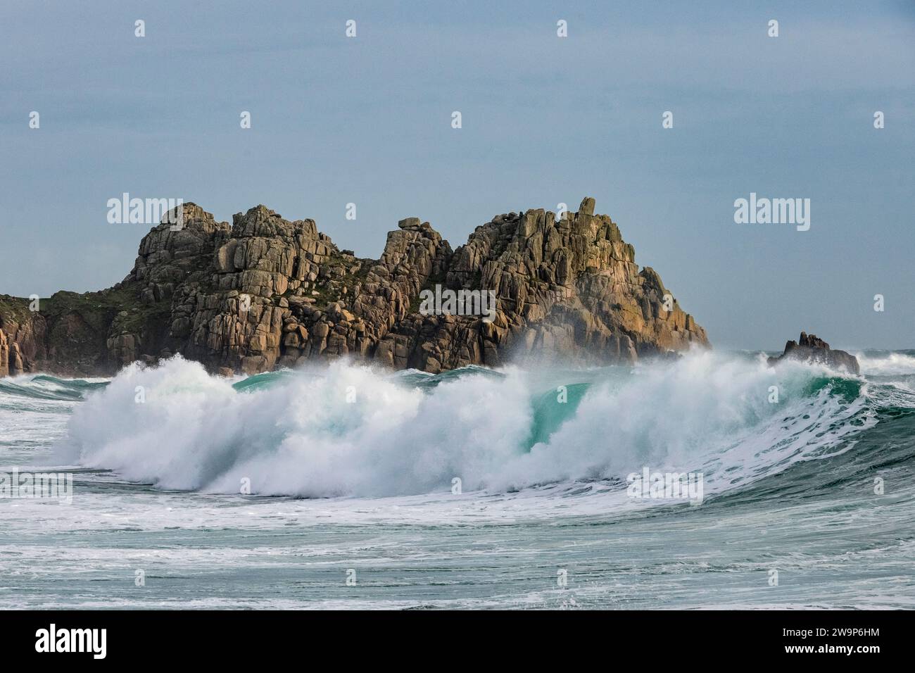 Grandi onde che si infrangono sulla spiaggia di Porthcurno, in Cornovaglia, con il Logan Rock sullo sfondo mentre Storm Gerrit passa per Natale 2023 Foto Stock