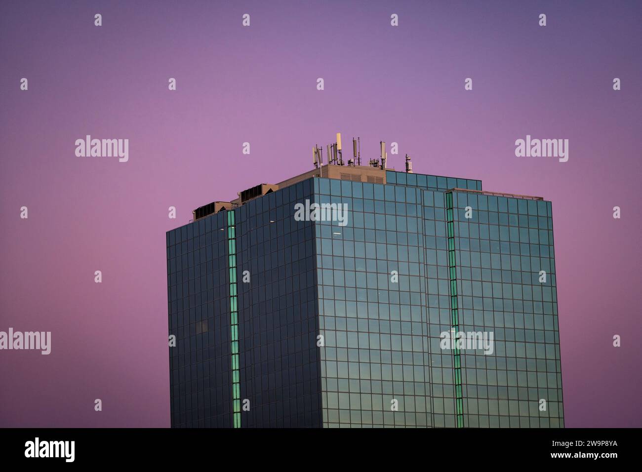 Torre verde di vetro per uffici adagiata contro il cielo rosso al crepuscolo. Foto Stock