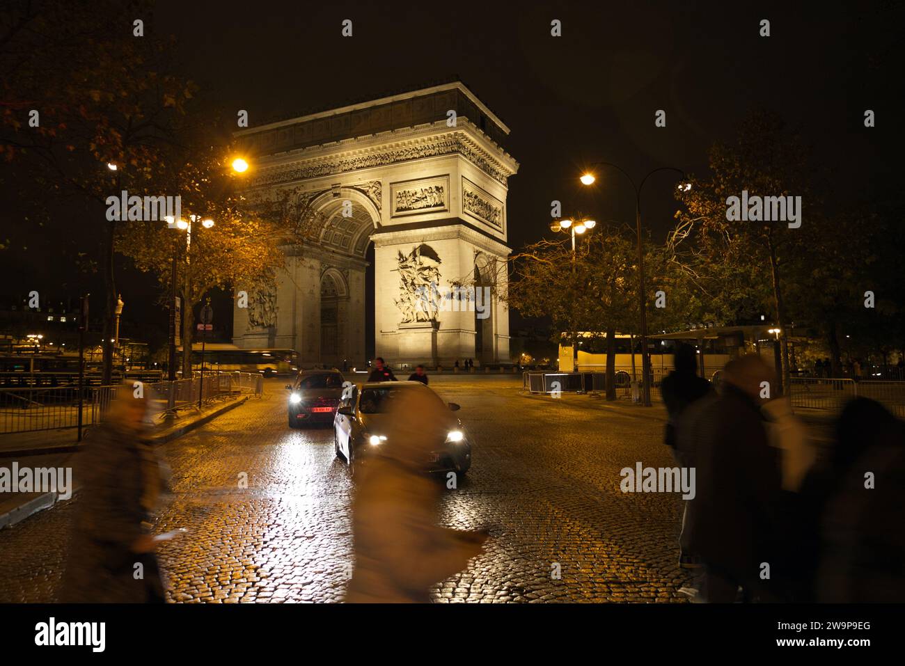 Place Charles de Gaulle o Place de l'Étoile, Parigi, Francia - Arc de Triomphe di notte con persone che attraversano la strada di fronte ad auto in avvicinamento Foto Stock