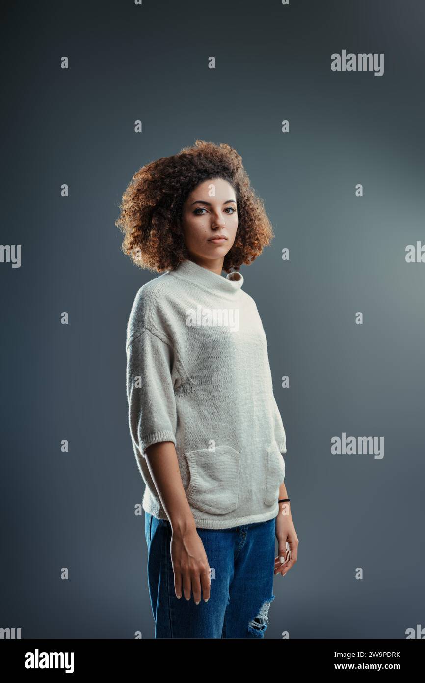 Riflessivo e calmo, lo sguardo morbido della donna e i capelli ricci raccontano una storia di quiete forza Foto Stock