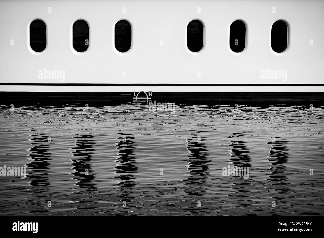 Finestre sul lato dello scafo di uno yacht che si riflettono su una superficie dell'acqua leggermente distorta. Foto Stock