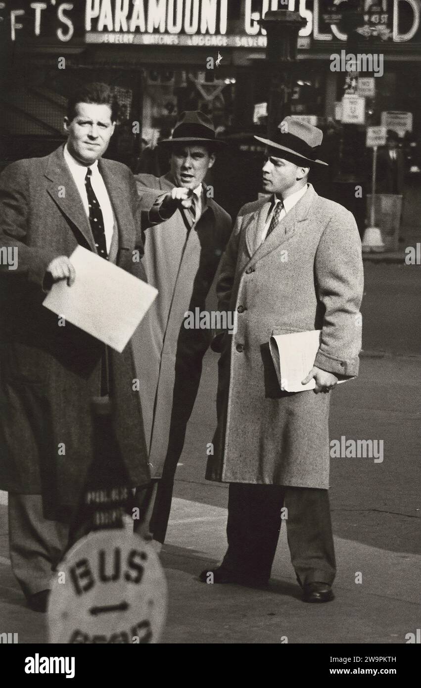 Tre uomini d'affari in soprabiti che parlano sul marciapiede, due tengono i giornali mentre un uomo al centro sta puntando il dito, West 43rd Street, New York City, New York, USA, Angelo Rizzuto, Anthony Angel Collection, novembre 1953 Foto Stock