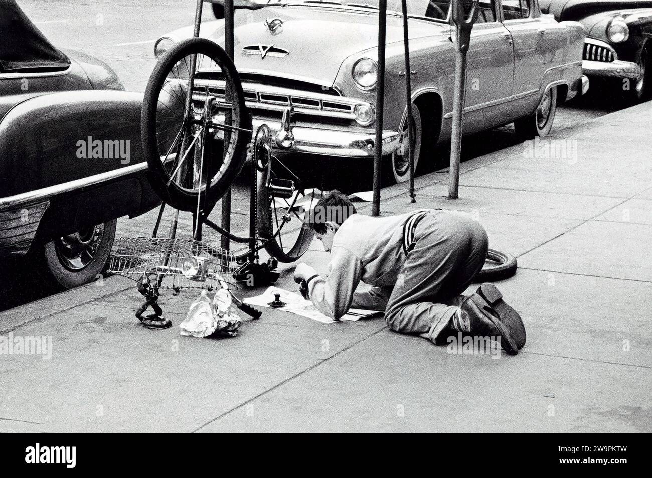 Uomo che fissa la bicicletta sul marciapiede, New York City, New York, USA, Angelo Rizzuto, Anthony Angel Collection, maggio 1954 Foto Stock