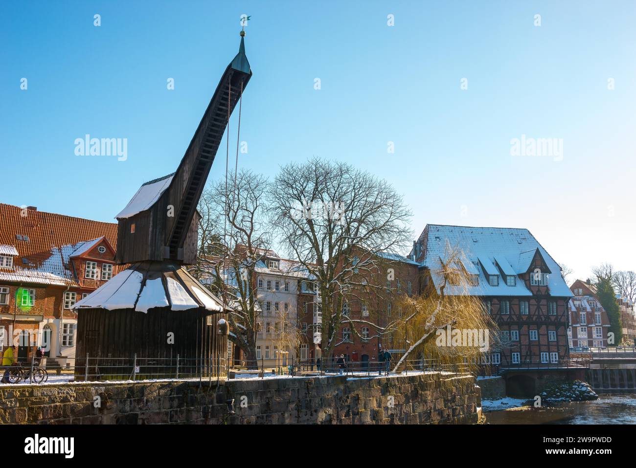 Soleggiata giornata invernale con cielo blu, vista della vecchia gru e degli edifici innevati sul fiume Ilmenau, alte Abtsmuehle, Hotel Bergstroem, alberi antichi Foto Stock