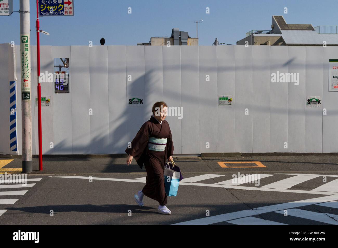 Una donna che indossa un kimono tradizionale attraversa una strada vicino al muro di un cantiere edile a Seijogakuenmae, Tokyo, Giappone. Foto Stock
