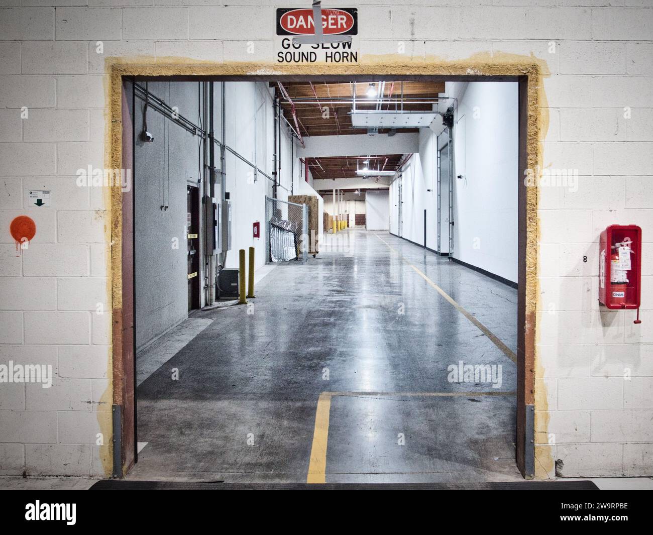 Apertura al corridoio di un magazzino industriale con pareti e pavimenti in cemento. Sguardo austero. Estintore e cartello "pericolo". Foto Stock