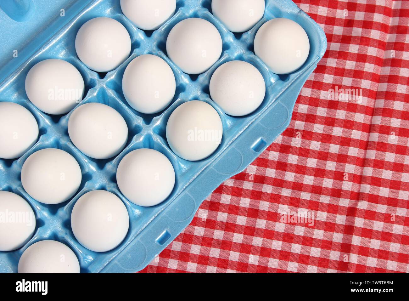 Cartone di uova su tavolo rustico con panno da tavolo a scacchi rosso Foto Stock