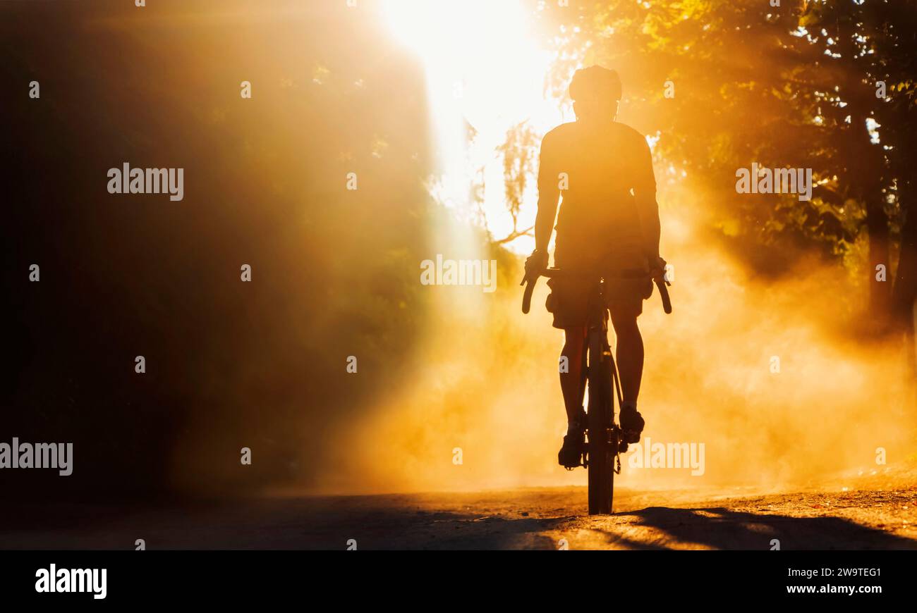 Silhouette di ciclista che corre su un sentiero in una nuvola di polvere al tramonto. Messa a fuoco morbida. Foto Stock