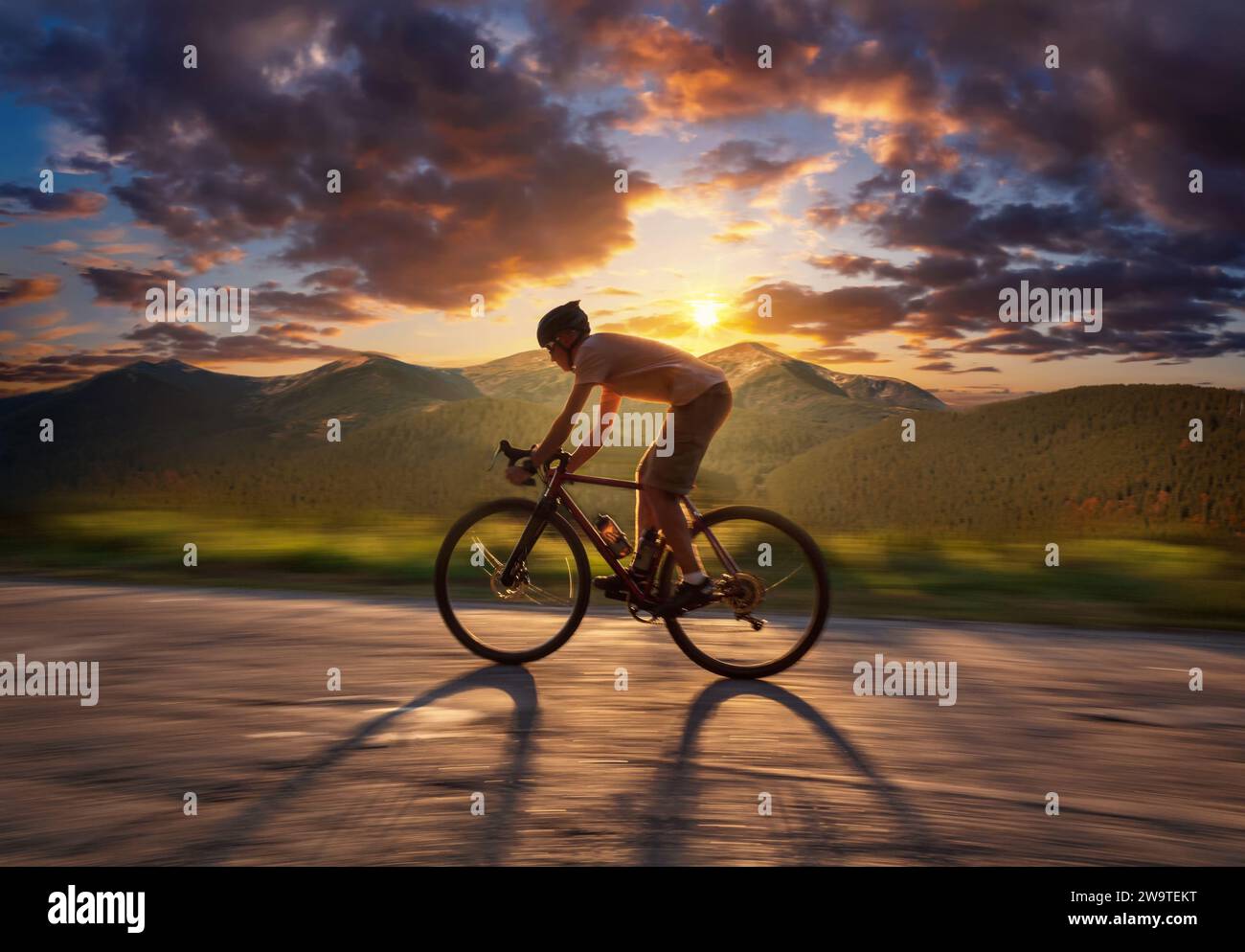Ciclista che corre su una strada di montagna al tramonto. Bellissimo paesaggio di uomini in bicicletta su strada asfaltata su splendide montagne sullo sfondo con spettacolo Foto Stock